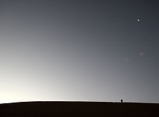ペルーの夕暮れの砂漠に輝く月とたたずむ人